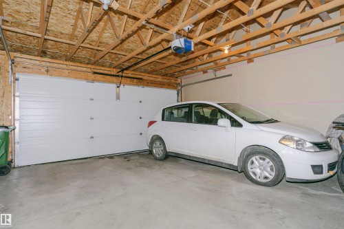Spacious garage with exposed wood rafters, a white sectional garage door, concrete flooring, and an automatic garage door opener - 11619 125 Street, Edmonton, AB 
