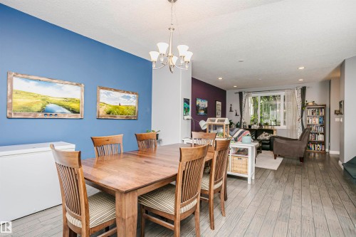 Open-concept living area with wood-finish flooring, a contemporary chandelier, and a large window providing natural light - 11619 125 Street, Edmonton, AB 
