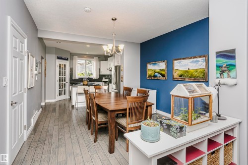 Open-concept dining and kitchen area featuring wood-finish flooring, a contemporary chandelier, a kitchen island with seating, dark countertops, and white cabinetry - 11619 125 Street, Edmonton, AB 