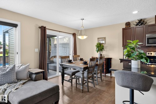Open-concept dining area featuring wood-finish flooring, a contemporary chandelier, and direct patio access through sliding glass doors - 12119 167A Avenue, Edmonton, AB 
