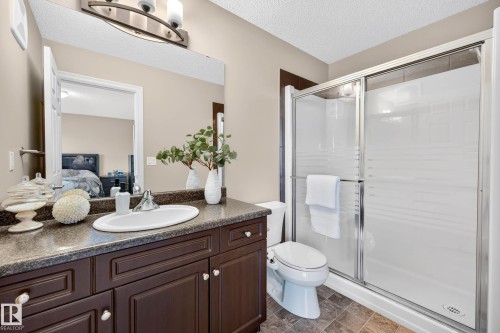 Bathroom featuring a dark wood-finish vanity with a built-in sink, a speckled countertop, a large wall-mounted mirror, and a glass-enclosed shower with frosted accents - 12119 167A Avenue, Edmonton, AB 