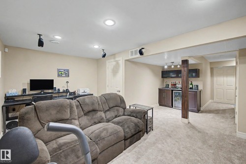 Finished lower level featuring recessed lighting, a built-in wet bar with dark cabinetry and stainless steel beverage cooler, light-toned carpeting, and a white paneled door - 12119 167A Avenue, Edmonton, AB 