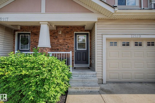 Entryway featuring a dark paneled door, stone facade accents, concrete steps, and a white porch railing - 12119 167A Avenue, Edmonton, AB 