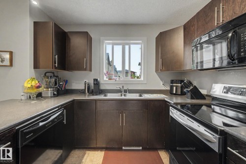 U-shaped kitchen featuring dark wood cabinetry, contrasting countertops, and a full suite of black and stainless steel appliances, including an over-the-range microwave - 25 12004 22 Avenue, Edmonton, AB - Indoor Photo Showing Kitchen With Double Sink