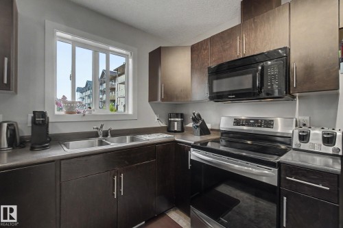 Kitchen featuring dark wood-finish cabinetry, a double basin stainless steel sink, and a stainless steel electric range with an overhead microwave - 25 12004 22 Avenue, Edmonton, AB - Indoor Photo Showing Kitchen With Double Sink