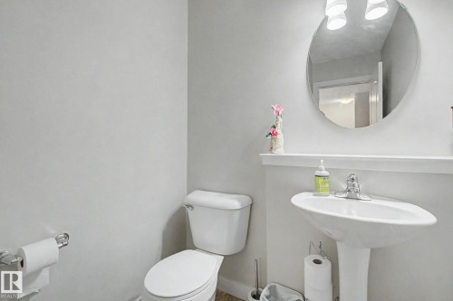 Bathroom featuring a pedestal sink with chrome faucet, a wall-mounted oval mirror, and a two-piece toilet - 25 12004 22 Avenue, Edmonton, AB - Indoor Photo Showing Bathroom