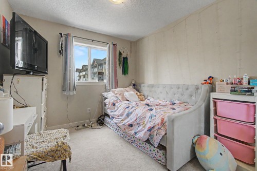 Carpeted room featuring a double-paned window, neutral wall paint, and a textured accent wall - 25 12004 22 Avenue, Edmonton, AB - Indoor Photo Showing Bedroom