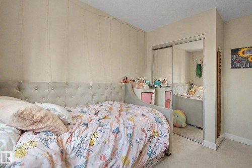 Bedroom featuring neutral wall tones, plush carpet flooring, a built-in closet with mirrored sliding doors, and crown molding - 25 12004 22 Avenue, Edmonton, AB - Indoor Photo Showing Bedroom