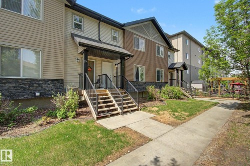 Multi-level townhome exterior featuring neutral-toned siding, dark stone accent cladding, and covered front entryways with black railings - 25 12004 22 Avenue, Edmonton, AB - Outdoor