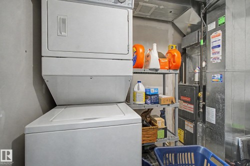 Dedicated laundry area featuring a stacked washer and dryer, adjacent shelving, and visible utility infrastructure - 25 12004 22 Avenue, Edmonton, AB - Indoor Photo Showing Laundry Room