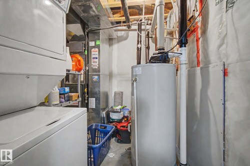 Dedicated utility area featuring a stacked washer and dryer, water heater, and exposed ceiling joists - 25 12004 22 Avenue, Edmonton, AB - Indoor Photo Showing Basement