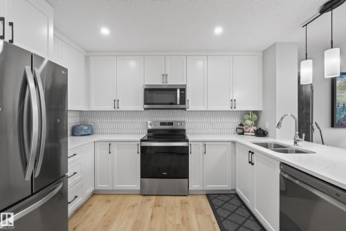 Kitchen featuring white shaker cabinetry, stainless steel appliances, light-toned wood-finish flooring, and pendant lighting - 5129 Lark Crescent, Edmonton, AB 