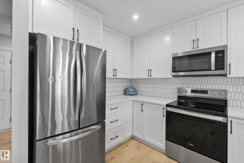 Contemporary kitchen featuring stainless steel appliances, white shaker cabinetry with dark hardware, quartz countertops, and a picket tile backsplash - 5129 Lark Crescent, Edmonton, AB 