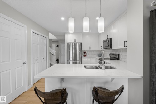 Contemporary kitchen featuring a dual basin sink, stainless steel appliances, and white cabinetry with dark hardware - 5129 Lark Crescent, Edmonton, AB 