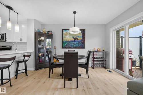 Open concept dining area featuring light wood-finish flooring, a contemporary pendant light fixture, and sliding glass doors providing access to an exterior deck - 5129 Lark Crescent, Edmonton, AB 