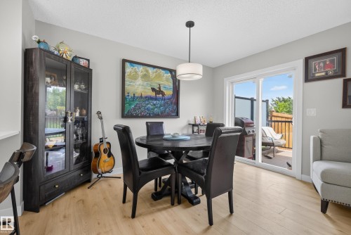 Dining area featuring wood-finish flooring, a contemporary pendant light fixture, and a sliding glass door leading to an outdoor deck - 5129 Lark Crescent, Edmonton, AB 