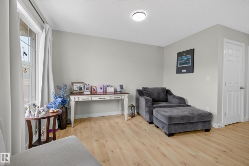 Spacious room featuring wood-finish flooring, a large window, light gray wall paint, and a paneled interior door - 5129 Lark Crescent, Edmonton, AB 