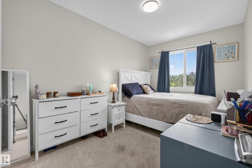 Bedroom featuring a window with natural light, light gray walls, textured carpet, and a flush mount ceiling light - 5129 Lark Crescent, Edmonton, AB 