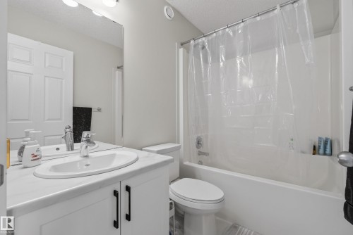 Full bathroom featuring a single vanity with an integrated sink, white cabinetry with black hardware, a mirror, and a toilet - 5129 Lark Crescent, Edmonton, AB 