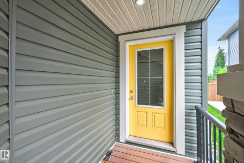 Vibrant yellow entry door with upper glass paneling, set against horizontal grey siding - 5129 Lark Crescent, Edmonton, AB 