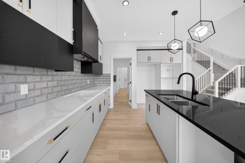 Modern kitchen featuring two-tone cabinetry, light wood-finish flooring, and a subway tile backsplash - 803 30 Avenue, Edmonton, AB 