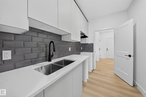 Modern kitchen featuring white flat-panel cabinetry, a dark subway tile backsplash, and light wood-finish flooring - 803 30 Avenue, Edmonton, AB 