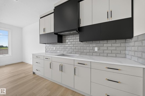 Contemporary kitchen featuring light gray and black cabinetry with gold-tone hardware, white countertops, and a gray subway tile backsplash - 803 30 Avenue, Edmonton, AB 