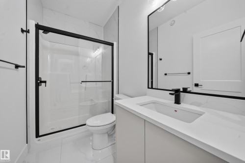 Bathroom featuring a white shower with a black-framed glass enclosure, white tile flooring, a single vanity with a white countertop and integrated sink, a black faucet, and a black-framed mirror - 803 30 Avenue, Edmonton, AB 