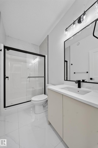Contemporary bathroom featuring a spacious shower with black-framed glass enclosure, white rectangular vanity with integrated sink, matte black faucet, and large wall-mounted mirror - 803 30 Avenue, Edmonton, AB 