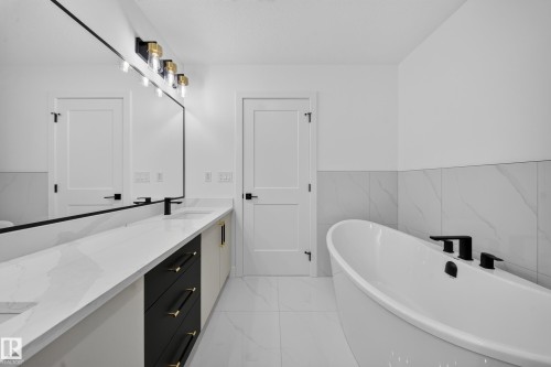 Contemporary bathroom featuring a freestanding soaking tub with matte black fixtures, a dual vanity with a white countertop and contrasting cabinetry, a large wall-mounted mirror, and gold and black lighting - 803 30 Avenue, Edmonton, AB 