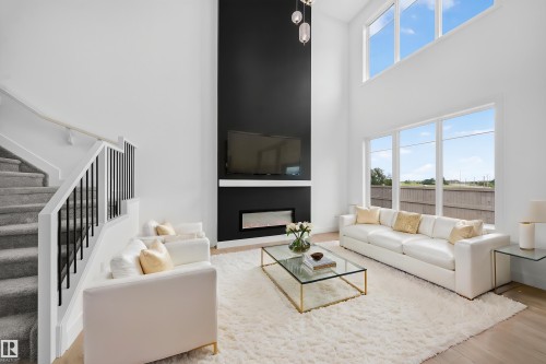 Two-story living area featuring a dramatic fireplace with a black accent wall, an integrated linear electric fireplace, and a wall-mounted television - 803 30 Avenue, Edmonton, AB 
