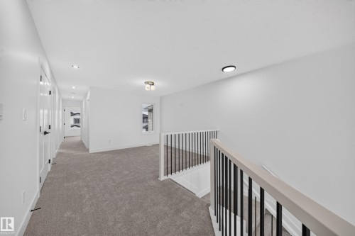 Upper-level landing featuring plush gray carpeting, white walls, and a contemporary black metal baluster railing with a light-toned wooden handrail - 803 30 Avenue, Edmonton, AB 
