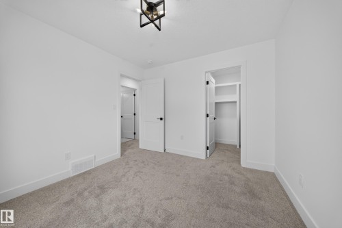 Neutral-toned carpeting throughout this space, featuring white walls, white trim, and a modern black and gold ceiling fixture - 803 30 Avenue, Edmonton, AB 