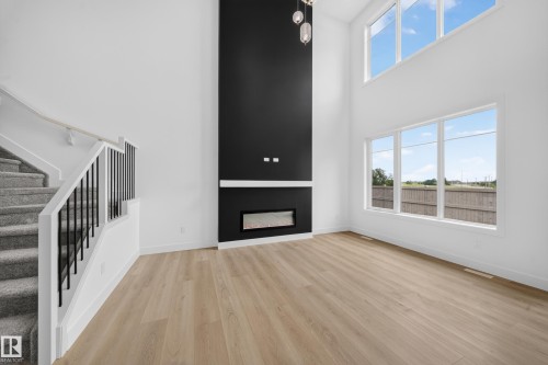 Open-concept living space featuring high ceilings, wood-finish flooring, and a contemporary linear fireplace with a black accent wall - 803 30 Avenue, Edmonton, AB 
