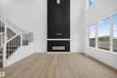 Two-story living area featuring a full-height black accent wall with an integrated linear fireplace, light wood-finish flooring, and a contemporary staircase with black iron spindles - 803 30 Avenue, Edmonton, AB 