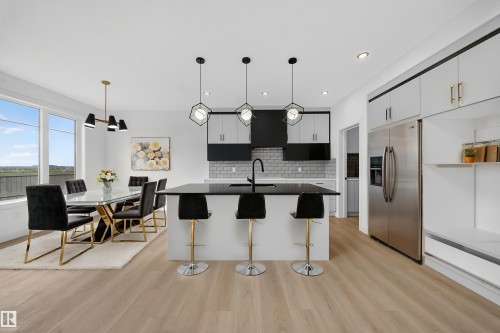 Open-concept kitchen and dining area featuring light wood-finish flooring, a kitchen island with pendant lighting, a subway tile backsplash, stainless steel appliances, and large windows - 803 30 Avenue, Edmonton, AB 