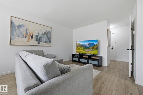 Open-concept living space featuring wood-finish flooring, white walls, and contemporary black door hardware - 105 16428 109 Street, Edmonton, AB 
