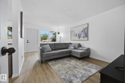 Living area featuring wood-finish flooring, white walls, and multiple windows allowing natural light - 
