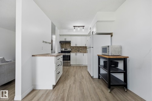 Contemporary kitchen featuring white cabinetry, a stone-look backsplash, stainless steel appliances, wood-finish flooring, and a track lighting fixture - 105 16428 109 Street, Edmonton, AB 