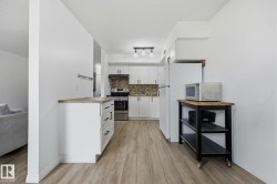 Contemporary kitchen featuring white cabinetry, a stone-look backsplash, stainless steel appliances, wood-finish flooring, and a track lighting fixture - 