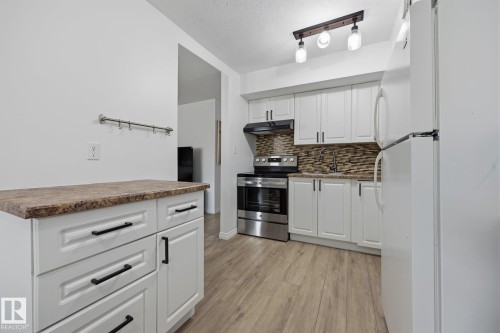 Modern kitchen featuring white cabinetry, wood-finish flooring, a mosaic tile backsplash, and stainless steel appliances - 105 16428 109 Street, Edmonton, AB 