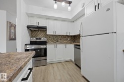 Galley kitchen featuring white cabinetry with matte black hardware, stainless steel appliances, mosaic tile backsplash, wood-finish flooring, and a peninsula with a stone-look countertop - 