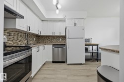 Modern kitchen featuring white cabinetry, a mosaic tile backsplash, wood-finish flooring, and stainless steel appliances including an oven range and dishwasher - 
