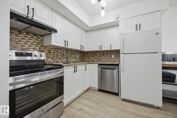 Kitchen featuring white cabinetry with dark hardware, a tile backsplash, and light-toned wood-finish flooring - 
