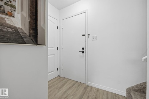 Entryway featuring light wood-finish flooring, white walls, and a white door with matte black hardware - 105 16428 109 Street, Edmonton, AB 