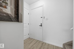 Entryway featuring light wood-finish flooring, white walls, and a white door with matte black hardware - 