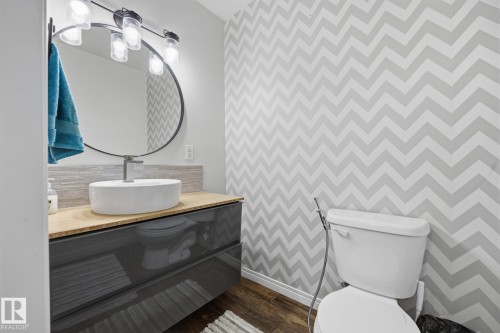 Powder room featuring a sleek floating vanity with a vessel sink, a contemporary round mirror, and a modern light fixture with clear glass shades - 105 16428 109 Street, Edmonton, AB 