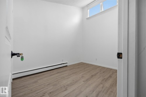 Room featuring wood-finish flooring, white baseboards, and a high transom window - 105 16428 109 Street, Edmonton, AB 