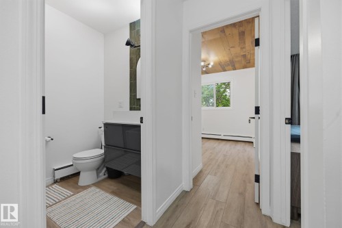Hallway featuring wood-finish flooring, white baseboards, and matte black door hardware - 105 16428 109 Street, Edmonton, AB 