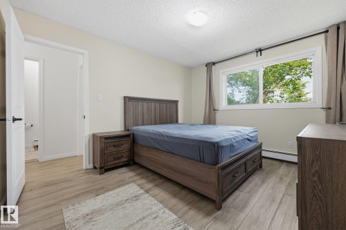 Bedroom featuring light wood-finish flooring, a bright window with neutral drapes, and a white ceiling with a flush-mount light fixture - 105 16428 109 Street, Edmonton, AB 